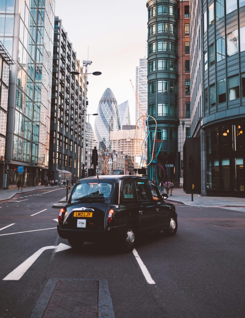 Classic black taxi navigating the streets of London with iconic skyscrapers in the background.