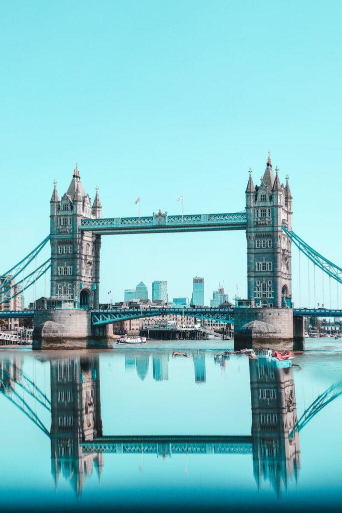 Beautiful image of Tower Bridge in London reflecting on the Thames River under a clear sky.