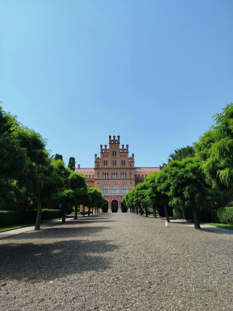 View of the Neo-Gothic building of Chernivtsi University surrounded by lush trees on a sunny day.