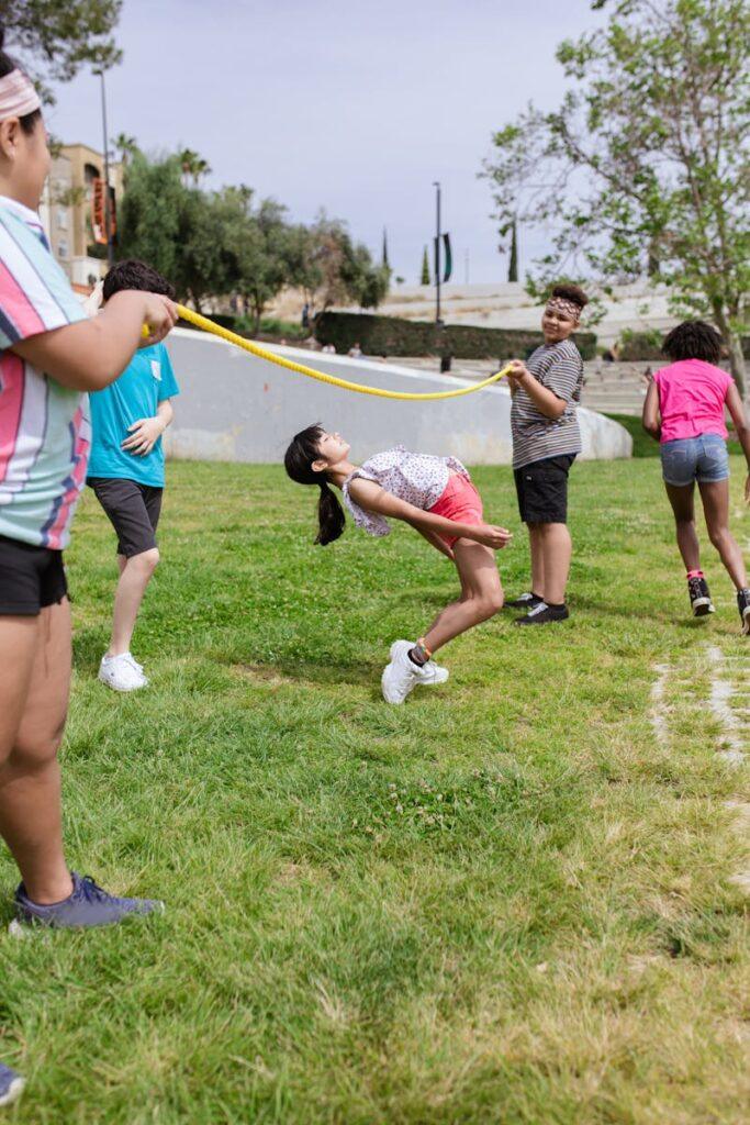 Group of kids enjoying limbo game during a summer camp in the park, fostering fun and teamwork.
