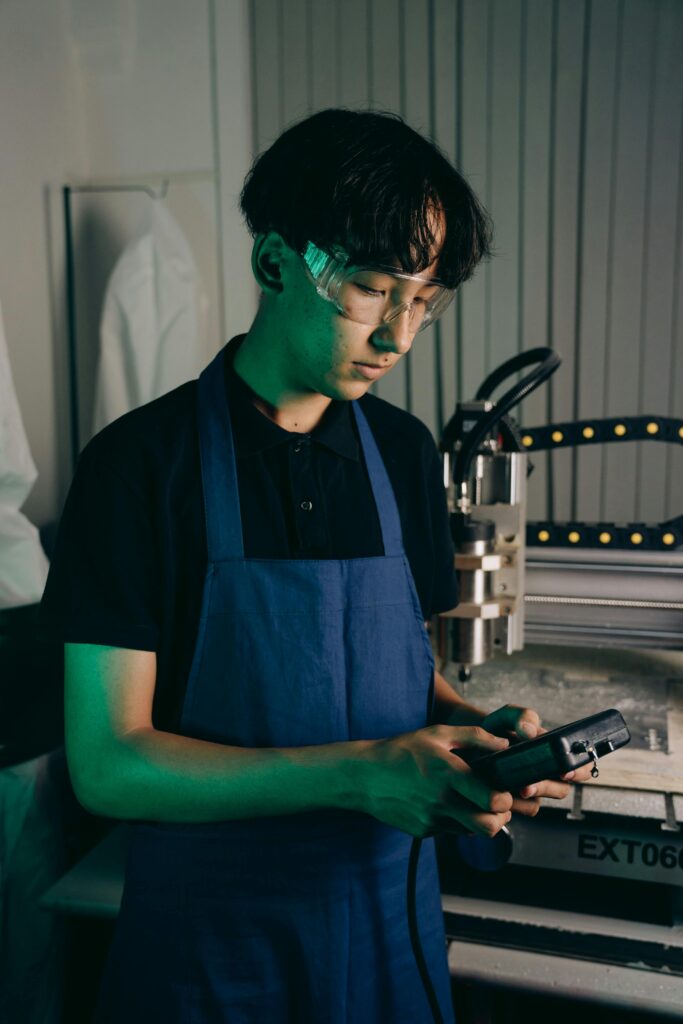 Asian male engineer working with machinery indoors wearing safety glasses and apron.