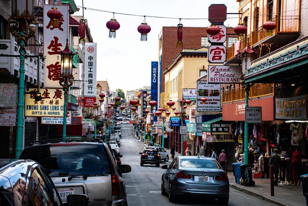 Bustling Chinatown street with hanging lanterns, shops, and vehicles.