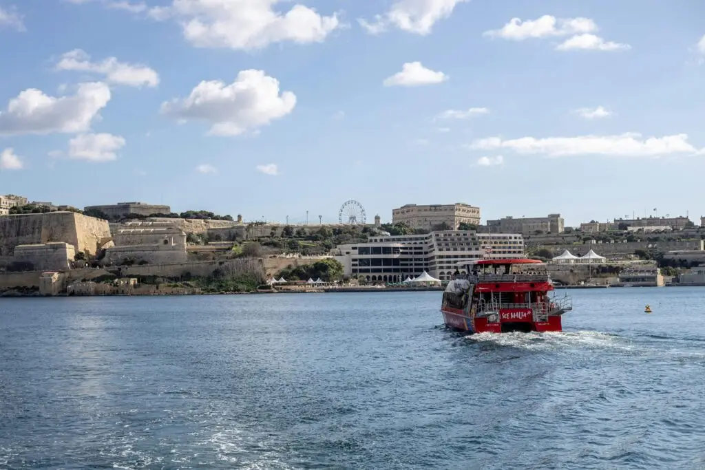 A ferry sails away from Valletta, Malta's historic coastal city under a bright sky.