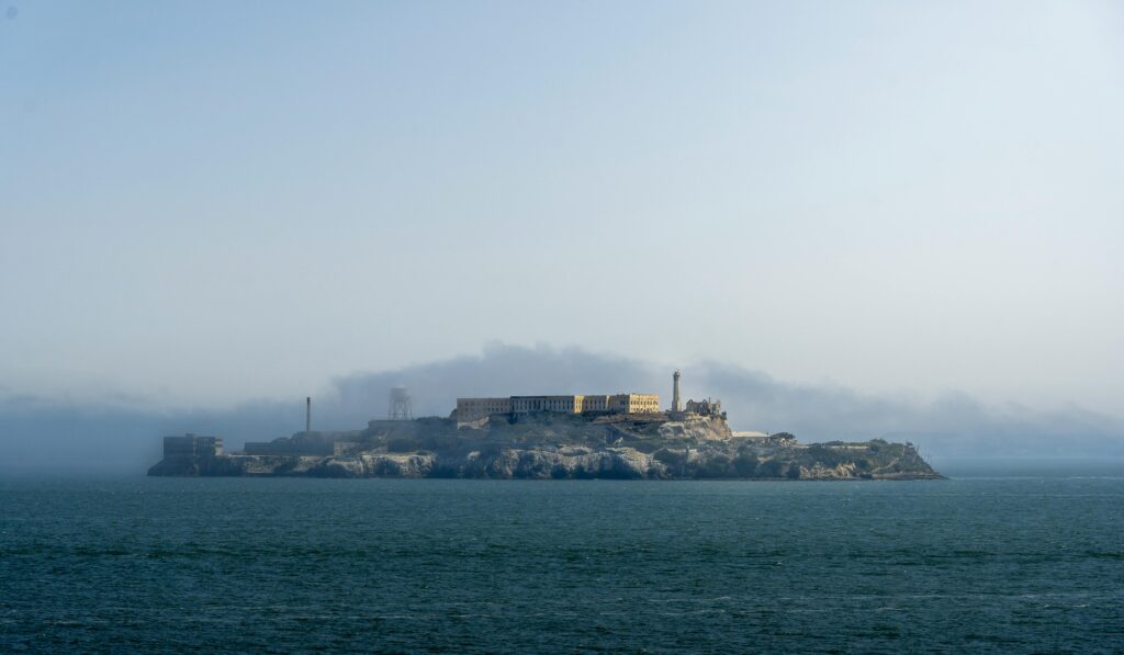 A serene view of Alcatraz Island silhouetted against a cloudy sky in San Francisco Bay.