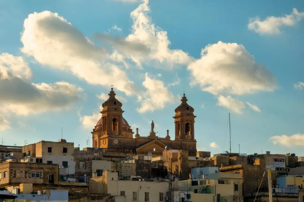 A scenic view of a Maltese basilica against a backdrop of scattered clouds in a blue sky.