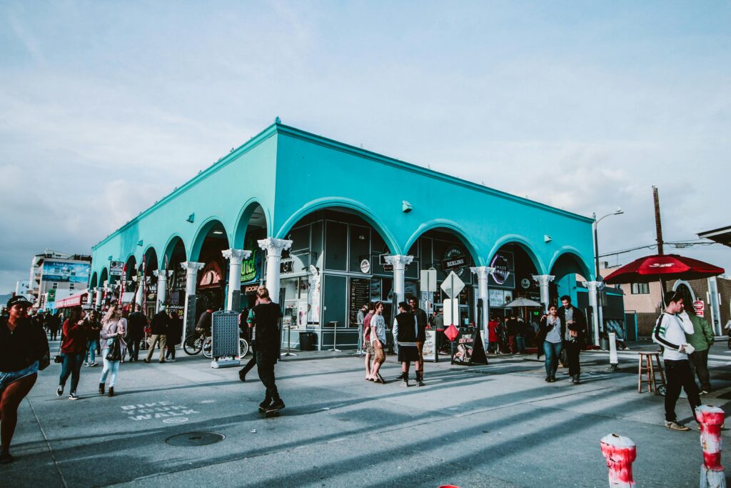 Lively street scene at Venice Beach with people enjoying the colorful architecture under a sunny sky.