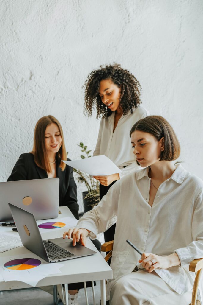 Three diverse businesswomen collaborating around laptops and documents in a modern office setting.