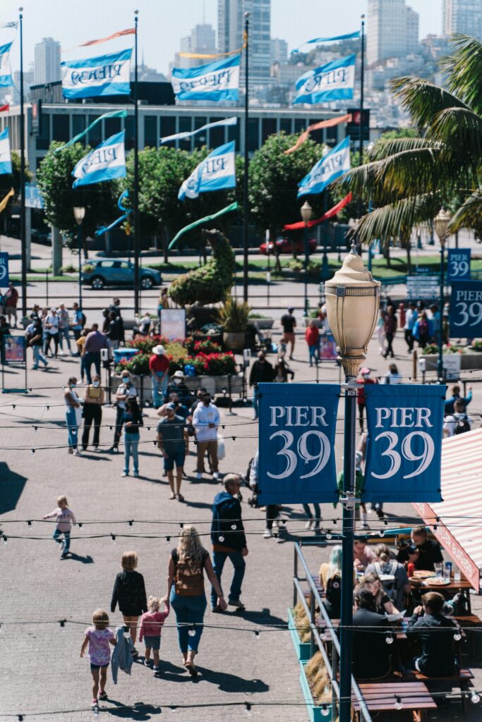 Lively pedestrian scene at Pier 39 with iconic banners and bustling atmosphere in San Francisco.