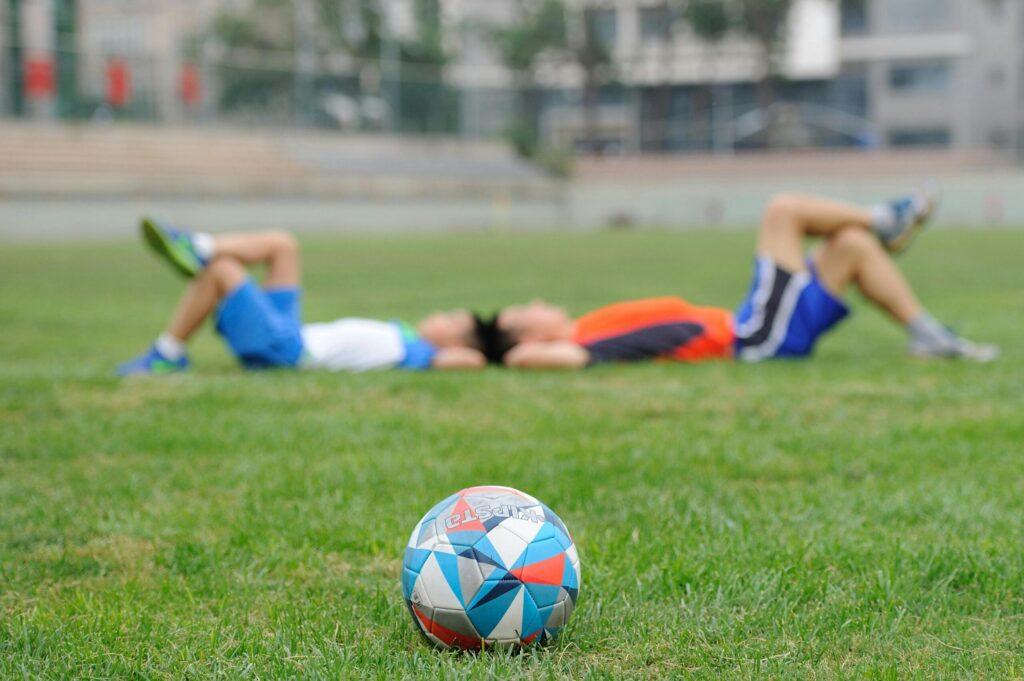 Two teenagers lying on grass near a soccer ball, enjoying leisure time outdoors.